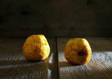 Sert yan lambanın altında, ahşap masada iki çürük elma, kontrastla savaşır.