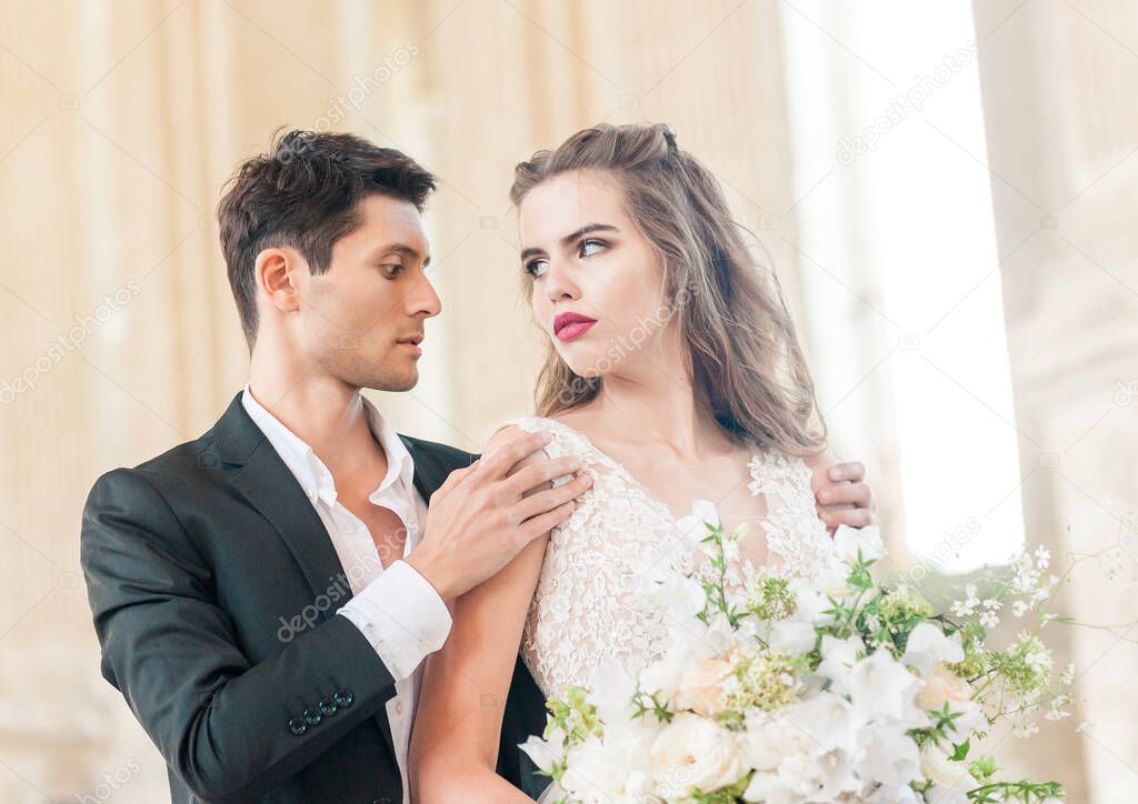 Closeup Portrait of wedding young bride and groom with bouquet posing by the old cathedral. Honeymoon couple kissing at wedding day, happy couple in love, wedding kiss