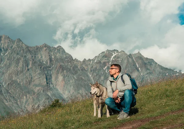 Attraktiv sportig man med husky tillsammans njuter av bergslandskap Royaltyfria Stockfoton