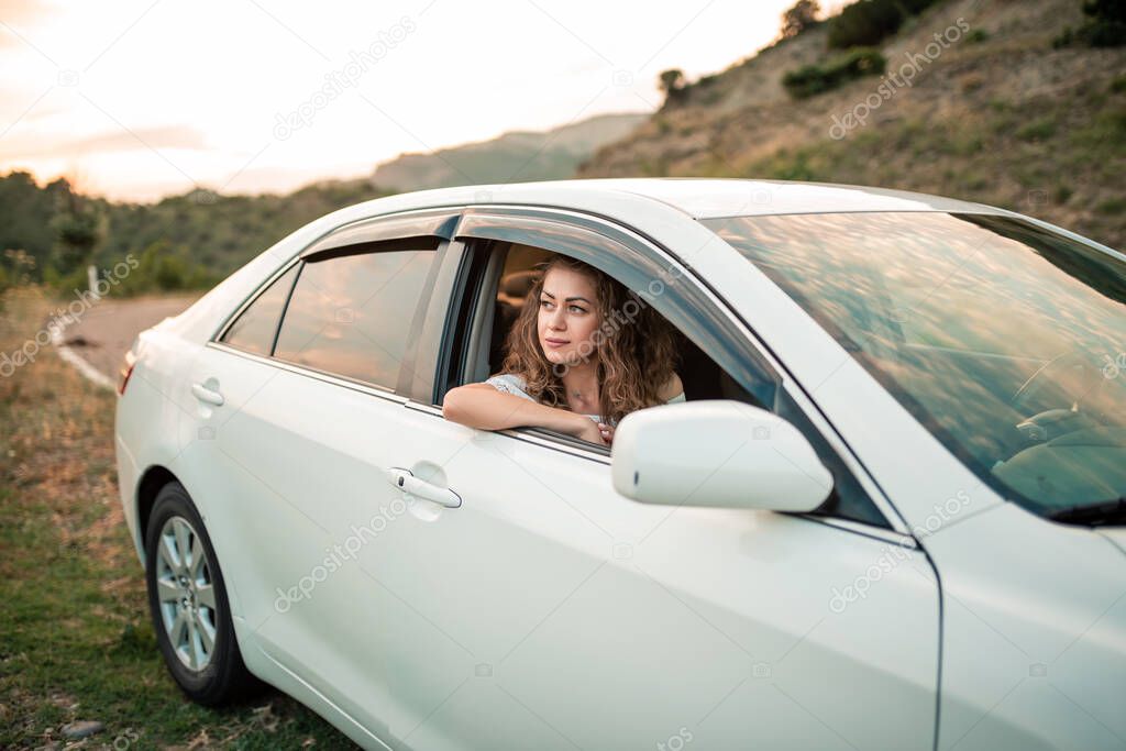 Young curly lovely girl driving a white car outdoors