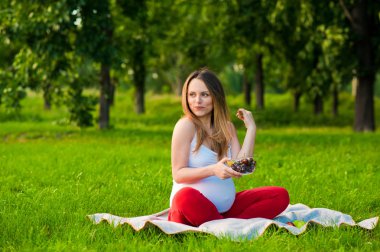 Çimenlerin üzerinde oturan genç hamile kadın