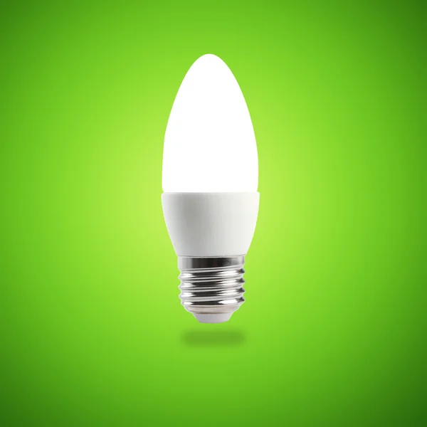 Lâmpada de poupança de energia LED brilhante em uma mão sobre um fundo verde — Fotografia de Stock