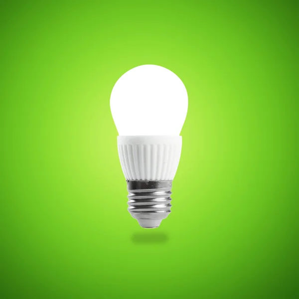 Lampadina a LED a risparmio energetico in una mano su sfondo verde — Foto Stock