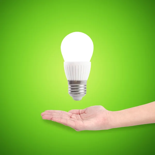 Bombilla de ahorro de energía led brillante en una mano sobre un fondo verde — Foto de Stock