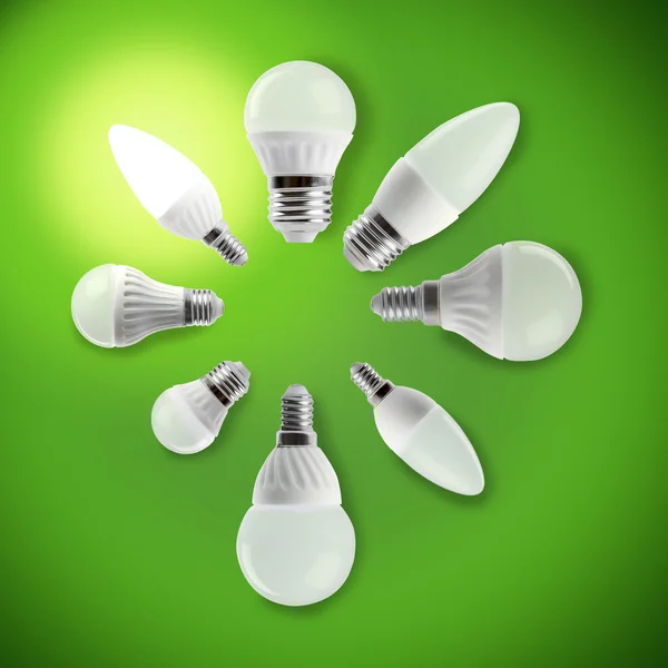 Bombilla de ahorro de energía led brillante en una mano sobre un fondo verde — Foto de Stock