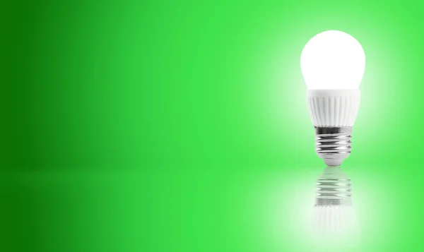 Bombilla de ahorro de energía led brillante en una mano sobre un fondo verde Imágenes de stock libres de derechos