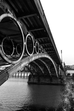 Black and  white photograph of the Isabel II bridge, better known as the Triana bridge (1852) that connects the center of Seville and the famous Triana neighborhood (Spain). View from below. clipart