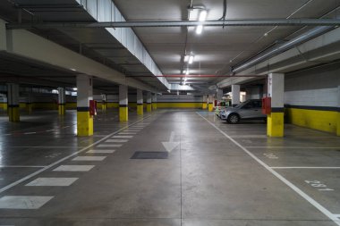 Tüp lambalı yeraltı garajı. Otoparkta hareket eden arabaların yönünü gösteren beyaz oklu bir şerit..