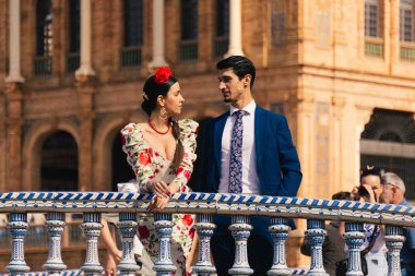 Seville, Spain; April 5th 2025: Woman wearing a flamenco dress looking into the eyes of a man in a suit. Couple dressed in the traditional outfit of the Seville Fair posing in the Plaza de Espana.