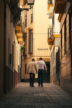 Seville, İspanya; 8 Haziran 2025: İki adam zarif giyinmiş eski Sevilla kasabasının dar sokaklarında yürüyorlar.