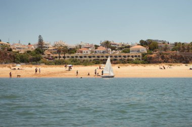 Portimao, Portekiz; 14 Haziran 2025: Portekiz kıyısındaki lüks bir konut kompleksi önünde plaj gününün tadını çıkaran turistler. Güneşli bir yaz gününde kalabalık olmayan plaj.