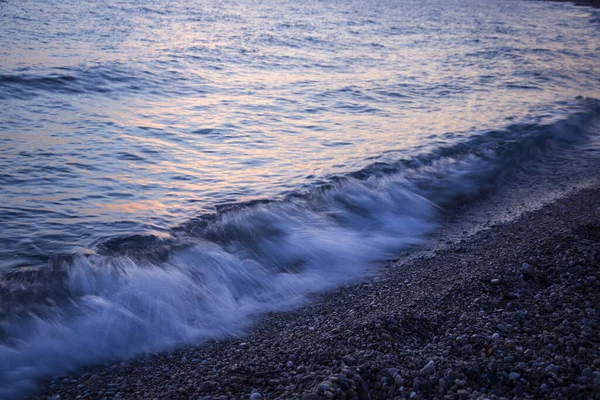 Gün Batımında Çakıl Taşlarının Üzerinde Mavi Deniz Dalgası — Stok fotoğraf