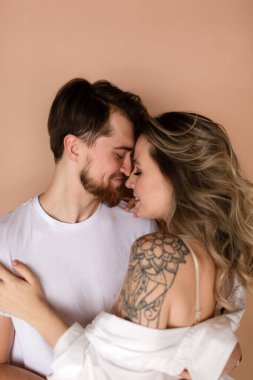 Bej arka planda kucaklaşan bir kadın ve erkeğin portresi. Gülümseyen çift. Romantik aşk. Beyaz gömlekli bir çift, çıplak omuzlu bir kadın..