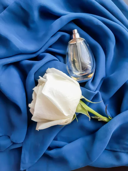 Beyaz gül ve parfüm şişesi açık mavi bir atkı üzerinde
