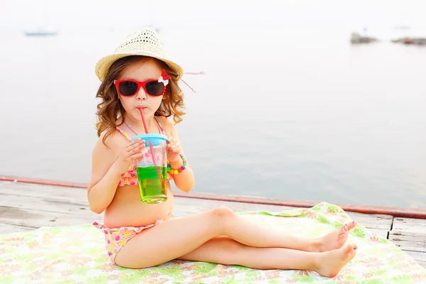 Маленька дівчинка п'є ігристу воду на пірсі — стокове фото
