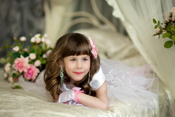 Das kleine Mädchen im Abendkleid auf dem Bett — Stockfoto