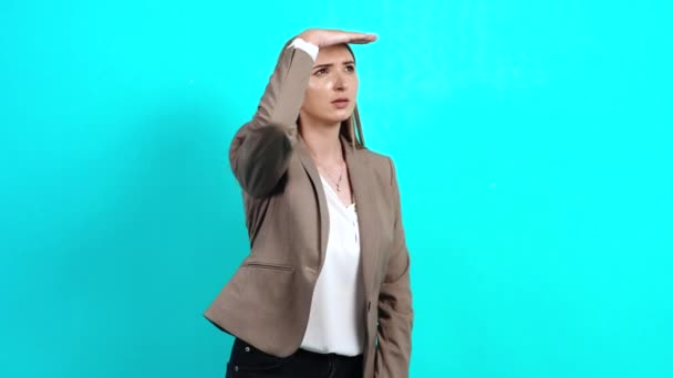 Curios tânără femeie atent în costum de afaceri, uitându-se departe, cu mâna deasupra capului ei — Videoclip de stoc