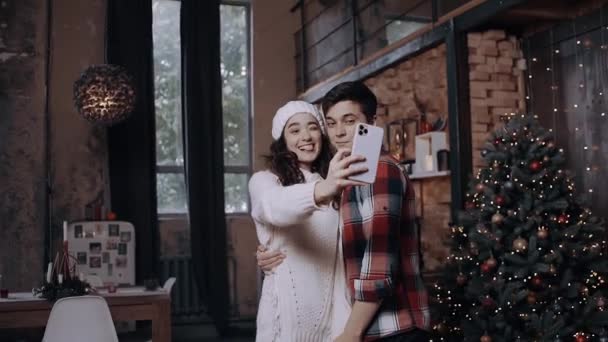 Young couple dressed in Christmas clothes, having fun and taking pictures with their phone near the Christmas — Stock Video