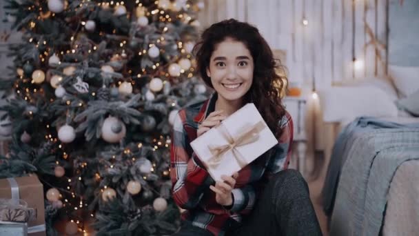 Retrato de una joven tiza muy bonita con un regalo en la mano junto al árbol de Navidad. — Vídeo de stock