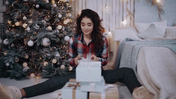 De krijtkleurige jonge vrouw speciaal gekleed voor de wintervakantie, zittend naast de kerstboom — Stockvideo