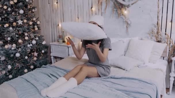 Die junge Frau, die auf dem Bett liegt, hat Spaß dabei, das Kissen hochzuwerfen. — Stockvideo
