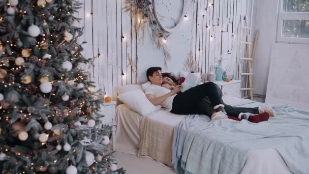 Fiatal romantikus pár fekszik az ágyon egy ajándékkal a kezében. — Stock videók