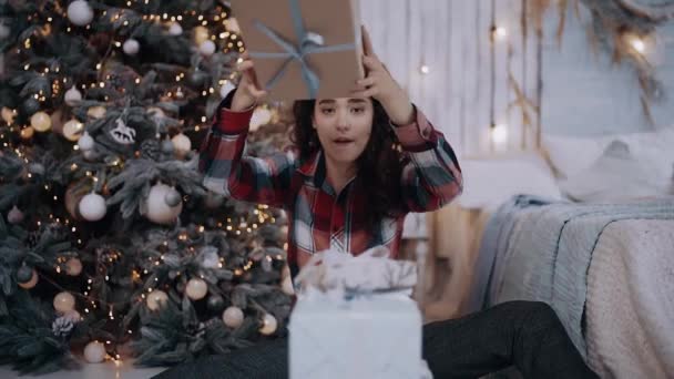 Porträt einer lustigen jungen Frau, die das letzte Geschenk neben den Weihnachtsbaum legt — Stockvideo
