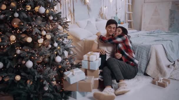 Het verliefde stel houdt elkaars hand vast naast de versierde kerstboom. — Stockvideo