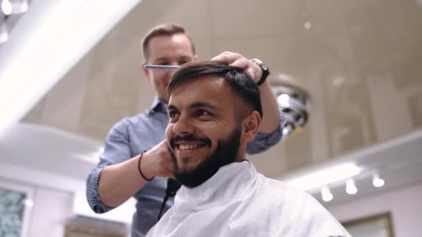 A businessman is preparing for a meeting. The miller arranges it with combs and a razor. The young man is very happy with his new hairstyle. He is a young man dressed in a classic style. — Stock Video