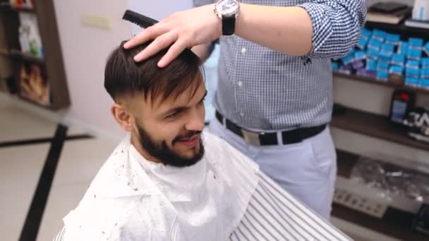 Junger Mann im Friseurladen sitzt in einem Sessel. Friseur schneidet sich mit Trimmer die Haare. — Stockvideo