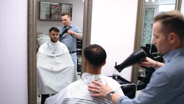 Egy energikus fiatalember meg akarja változtatni a frizuráját. A molnár a hajszárítóval szárítja a haját. A fiatalember nagyon elégedett a kapott eredménnyel.. — Stock videók