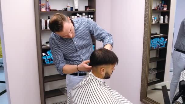 Un meunier compétent fait son travail. Avec la tondeuse à cheveux, il fait une coiffure de jeunes hommes. C'est un meunier avec beaucoup d'expérience et il connaît bien son travail. Le client est satisfait du résultat. — Video