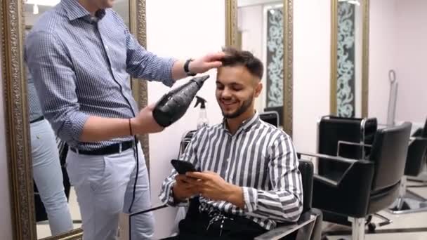 Geschäftsmann tätigt eine Transaktion am Telefon, während er beim Friseur eine neue Schneidemaschine herstellt — Stockvideo