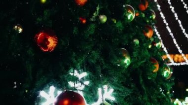 Kar yağarken güzelce dekore edilmiş dev bir köknar ağacının üzerinde bir sürü renkli kürenin olduğu videoyu kapat.