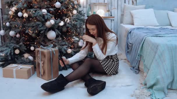 彼女の手で彼女の携帯電話でベッドの上に横たわって、冬の休日のために特に身を包んだ白亜紀の若い女性 — ストック動画