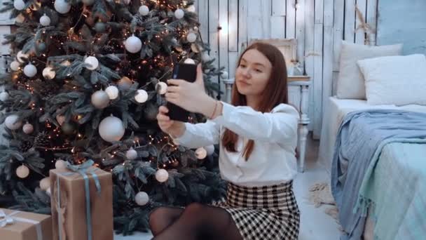 Молода жінка фотографує біля дерева вдома у вітальні — стокове відео