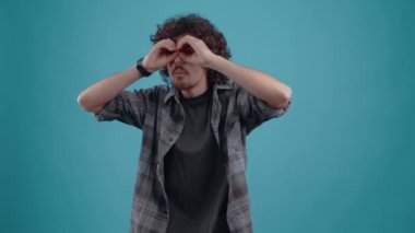 Hippi, elleri gözlerinde, iş arkadaşlarını gözetliyor. Kıvırcık saçlı genç