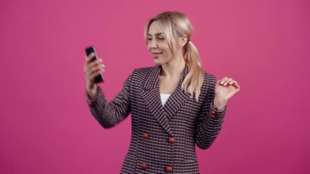Возбужденная и счастливая молодая женщина, держит телефон в руке и разговаривает онлайн с близкими, здоровается рукой и рада их видеть.. — стоковое видео