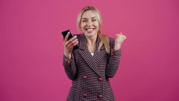 Überraschte und siegreiche junge Frau liest am Telefon, dass sie zur Gewinnerin eines Online-Wettbewerbs gewählt wurde, sie genießt und lächelt schön. — Stockvideo