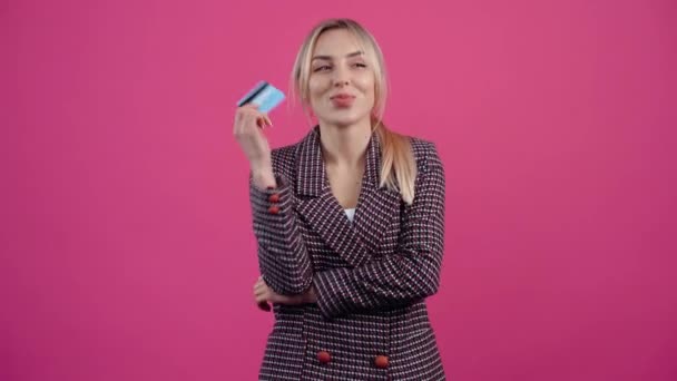 Podekscytowana młoda kobieta, z kartą kredytową w ręku, uśmiecha się szczęśliwie i myśli o nowych zakupach. — Wideo stockowe
