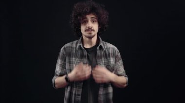 Genç adam, duygusal olarak şaşırmış, elleriyle kalbini hareket ettiriyor ve gülümsüyor..
