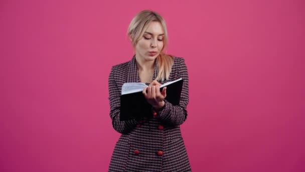 Murid yang lucu, catatan di buku harian, penasaran. Cantik muda pirang dalam jaket merah muda. — Stok Video