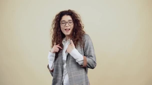이봐, 회색 재킷에 흰색 셔츠를 입은 곱슬곱슬 한 머리의 미친 여자 가 스튜디오의 베이지 배경에 고립된 안경을 쓰고 있는 미친 여자. — 비디오