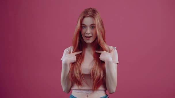 Boldog, vörös hajú, 20 éves fiatal nő, rózsaszín, alkalmi pólóban, rózsaszín háttérrel. A népek életmódjának fogalma — Stock videók