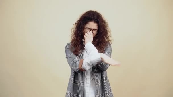 Mladá žena, která si neuvědomuje, jak páchne, si rukou položí ruku na nos a zamává. Křída v šedé bundě a bílé košili, s brýlemi pózujícími izolovaně na béžovém pozadí — Stock video