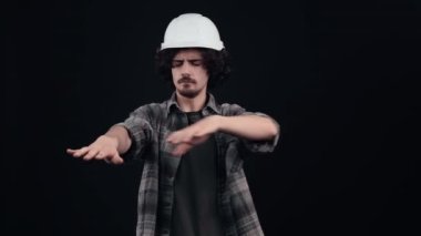 Elleri uzanmış, karanlıkta bir şeyler arayan kafası karışmış bir hippi. Kıvırcık saçlı genç adam kafasına ekose gömlek giymiş özel bir kask takıyor.,