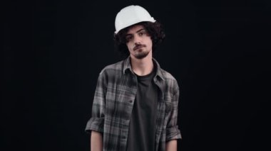 Genç mühendis parmaklarını alnına yakın tutarak, alaycı bir şekilde kaybettiğini gösteriyor. Kıvırcık saçlı genç adam kafasına özel bir kask takıyor, ekose gömlek giyiyor, siyah bir kask giyiyor.