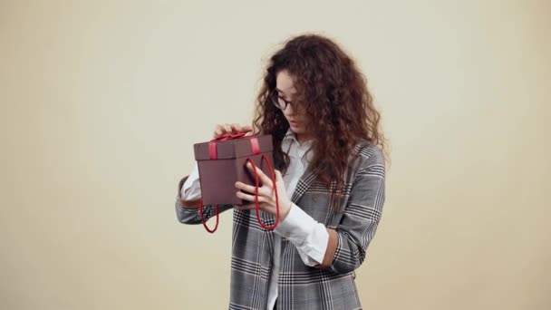 Η περίεργη νεαρή γυναίκα ανοίγει ένα κουτί δώρου και, έκπληκτη από αυτό που είναι μέσα στο κουτί, χαμογελάει με τα δόντια της. — Αρχείο Βίντεο
