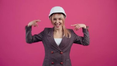 Mühendis kaskı takan mutlu genç kadın kameraya gülümsüyor pembe ceketli genç sarışın..