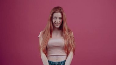 Kafası karışmış kızıl saçlı, eğilmiş, anlamıyor ve sonunda hoşnutsuz bir şekilde bir kez daha soruyor. 20 yaşında, çilli hippi pembe tişörtlü, pembe arka planda izole edilmiş..